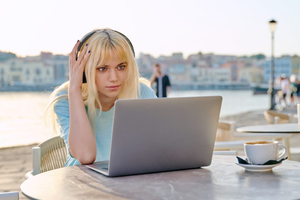 Surprised teenage female with headphones looking at laptop in outdoor cafe