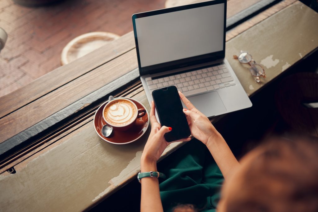 Phone, laptop and coffee shop with a woman customer browsing social media or texting from above. Co