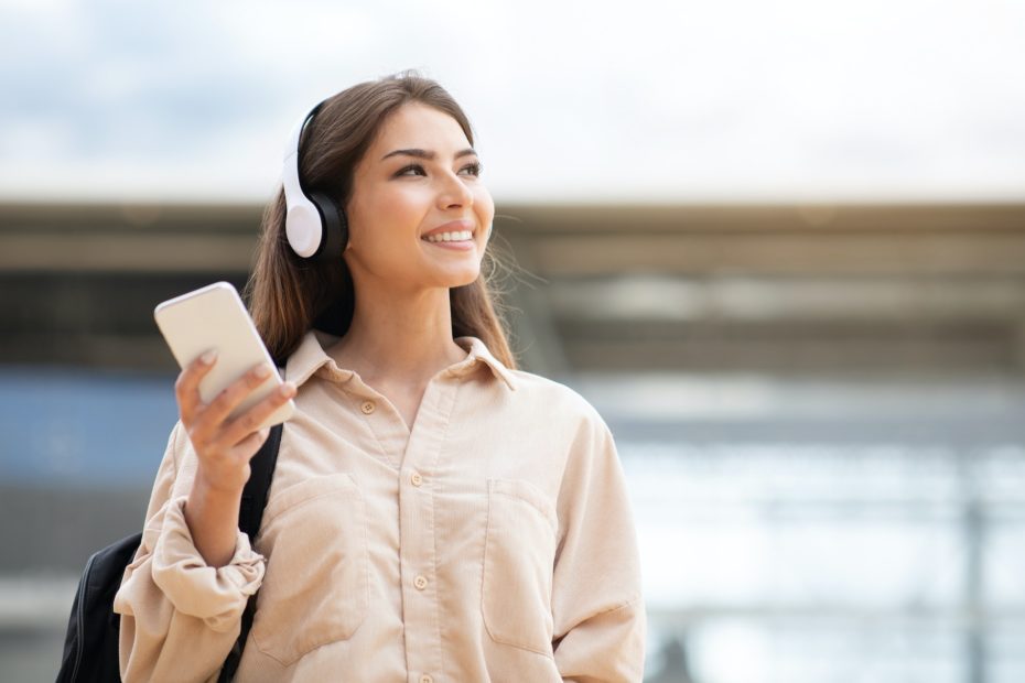 Lady with wireless headphones and mobile phone listening music outside